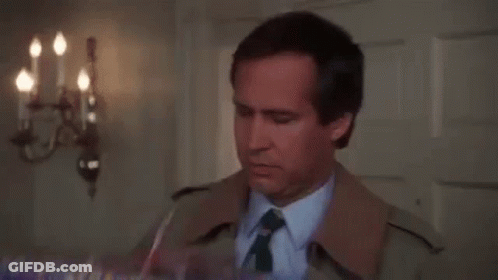 A Man In A Trench Coat And Tie Is Holding A Box Of Gifts . GIF