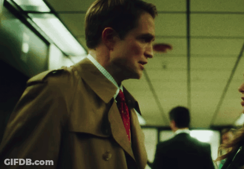 A Man In A Trench Coat And Tie Is Talking To Another Man GIF