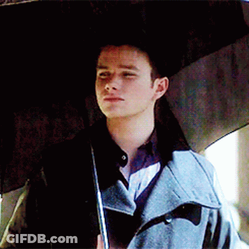 A Man In A Trench Coat Holds An Umbrella Over His Head GIF