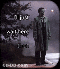 A Man In A Trench Coat Is Standing On A Sidewalk With The Words I 'Ll Just Wait Here Then GIF