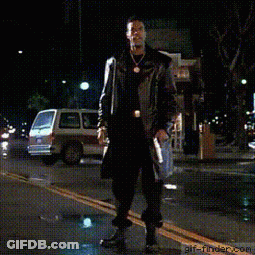 A Man In A Trench Coat Is Walking Down A Street At Night With His Arms Outstretched .. GIF