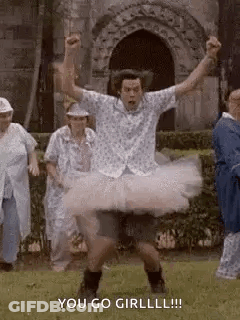 A Man In A Tutu Is Dancing In A Park With A Group Of People . GIF