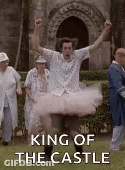 A Man In A Tutu Is Jumping In The Air In Front Of A Castle . GIF