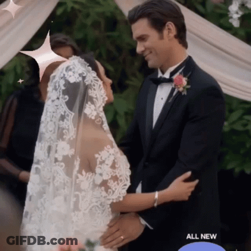 A Man In A Tuxedo And A Bride In A Wedding Dress Are Hugging GIF