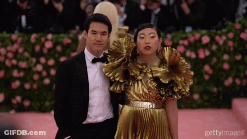 A Man In A Tuxedo And A Woman In A Gold Dress Pose For A Photo GIF