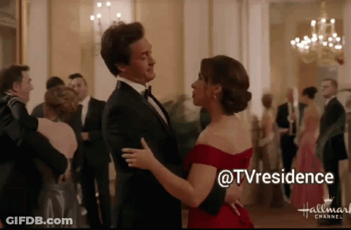 A Man In A Tuxedo And A Woman In A Red Dress Are Dancing In Front Of A Hallmark Channel Logo GIF