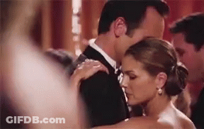 A Man In A Tuxedo And A Woman In A White Dress Are Dancing Together . GIF