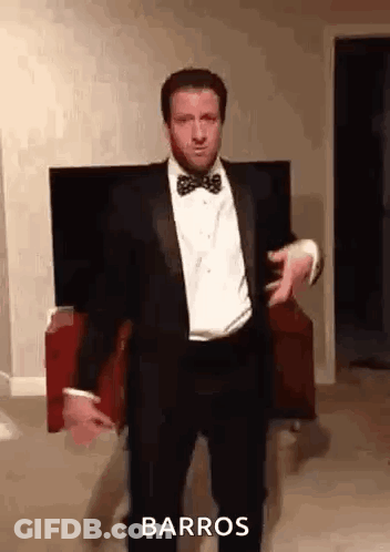 A Man In A Tuxedo And Bow Tie Is Dancing In Front Of A Television . GIF