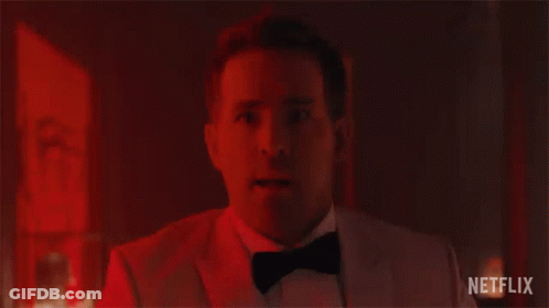 A Man In A Tuxedo And Bow Tie Is Looking At The Camera In A Dark Room . GIF