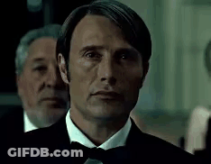 A Man In A Tuxedo And Bow Tie Is Looking At The Camera With Two Men Behind Him . GIF