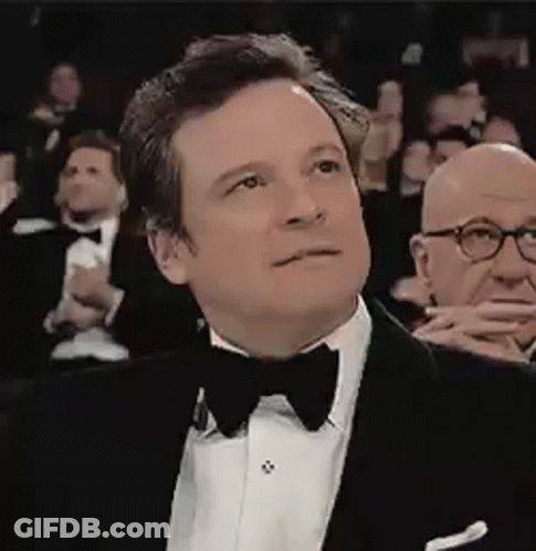 A Man In A Tuxedo And Bow Tie Is Sitting In Front Of A Crowd . GIF
