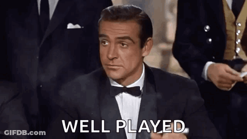 A Man In A Tuxedo And Bow Tie Is Sitting In Front Of A Group Of Men And Saying `` Well Played '' . GIF