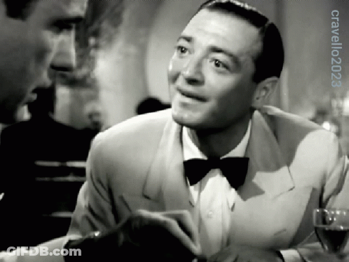 A Man In A Tuxedo And Bow Tie Is Smiling In A Black And White Photo GIF