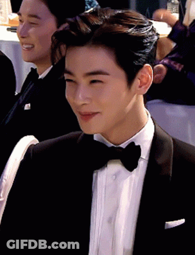 A Man In A Tuxedo And Bow Tie Is Smiling While Sitting At A Table GIF