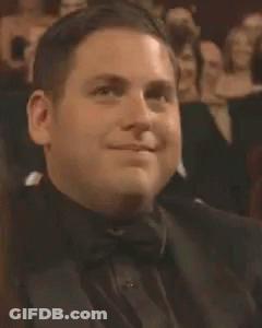 A Man In A Tuxedo And Bow Tie Is Smiling While Sitting In A Theatre . GIF