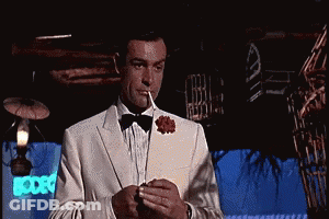 A Man In A Tuxedo And Bow Tie Is Smoking A Cigarette GIF
