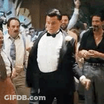 A Man In A Tuxedo And Bow Tie Is Standing In A Crowd Of Men . GIF