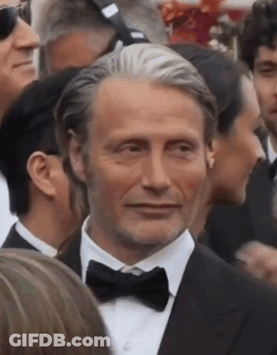 A Man In A Tuxedo And Bow Tie Is Standing In A Crowd Of People . GIF