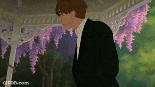 A Man In A Tuxedo And Bow Tie Is Standing In Front Of A Gazebo With Purple Flowers . GIF