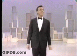 A Man In A Tuxedo And Bow Tie Is Walking On A Stage GIF