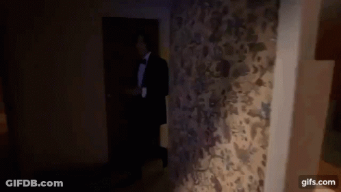 A Man In A Tuxedo And Bow Tie Is Walking Through A Doorway . GIF