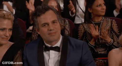 A Man In A Tuxedo And Bow Tie Sits In A Theatre Applauding GIF