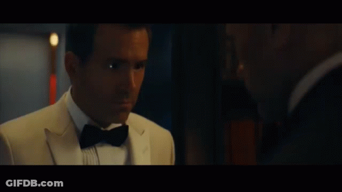 A Man In A Tuxedo And Bow Tie Talks To Another Man In A Suit GIF