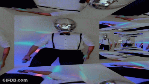 A Man In A Tuxedo And Suspenders Is Standing In A Room With A Disco Ball On His Head GIF