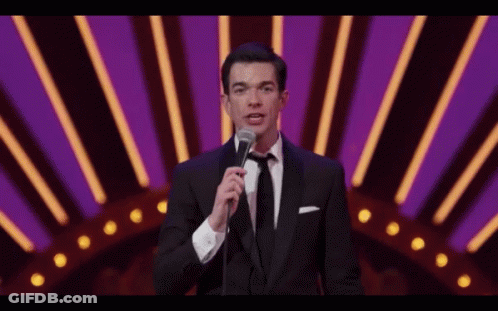 A Man In A Tuxedo And Tie Is Holding A Microphone GIF