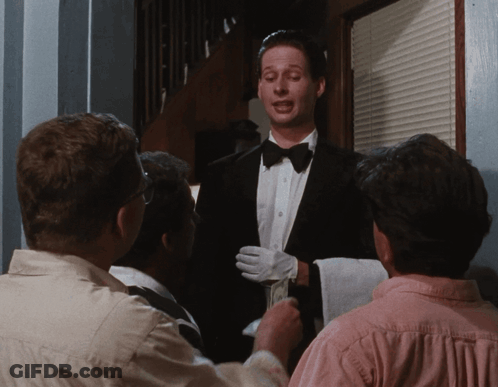 A Man In A Tuxedo And White Gloves Is Talking To A Group Of People GIF