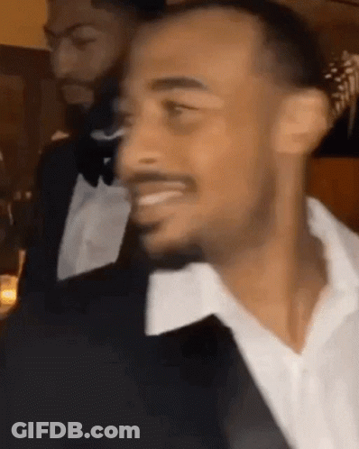 A Man In A Tuxedo And White Shirt Is Smiling At A Party . GIF