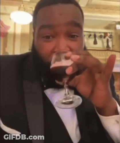 A Man In A Tuxedo Drinking A Glass Of Wine GIF