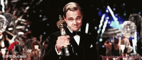A Man In A Tuxedo Holding An Oscar Statue GIF