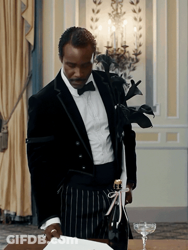 A Man In A Tuxedo Holds A Bottle Of Champagne With A Bow On It GIF