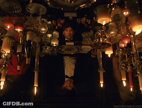 A Man In A Tuxedo Holds A Plate With A Candle On It In Front Of Candles GIF