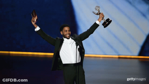 A Man In A Tuxedo Holds A Trophy In His Hands GIF