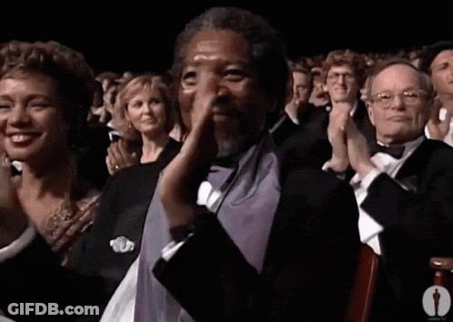 A Man In A Tuxedo Is Applauding In Front Of A Crowd Of People GIF