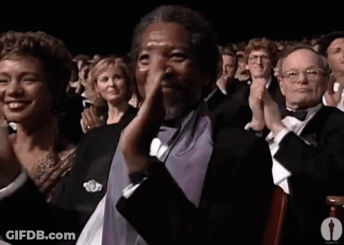 A Man In A Tuxedo Is Applauding In Front Of A Crowd GIF