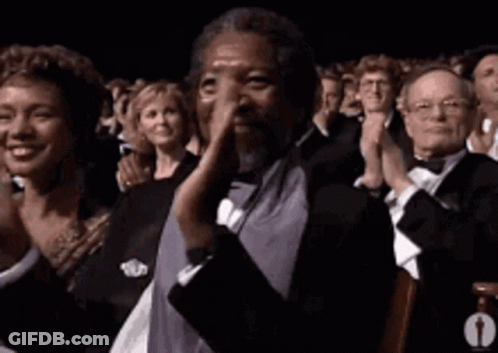 A Man In A Tuxedo Is Clapping His Hands In A Crowd Of People . GIF