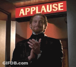 A Man In A Tuxedo Is Clapping In Front Of A Sign That Says Applause GIF