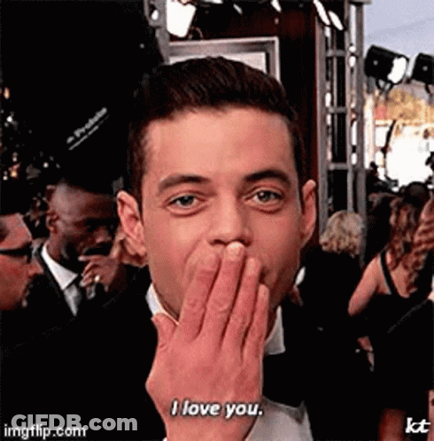 A Man In A Tuxedo Is Covering His Mouth With His Hand And Saying I Love You . GIF