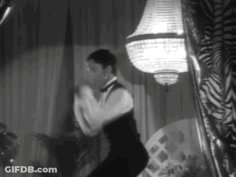 A Man In A Tuxedo Is Dancing In A Black And White Photo GIF