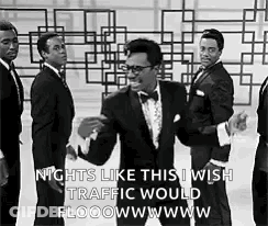 A Man In A Tuxedo Is Dancing In Front Of A Group Of Men . GIF