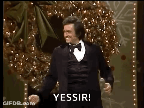 A Man In A Tuxedo Is Dancing On A Stage In Front Of A Christmas Tree While Holding A Microphone . GIF