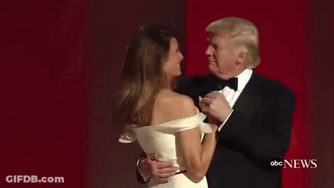 A Man In A Tuxedo Is Dancing With A Woman In A White Dress On A Red Carpet . GIF
