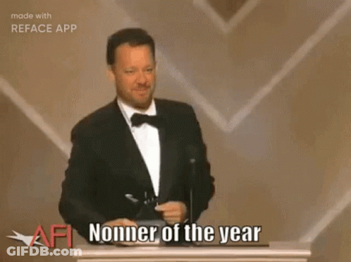 A Man In A Tuxedo Is Giving A Speech On A Stage In Front Of A Crowd And A Large Screen . GIF