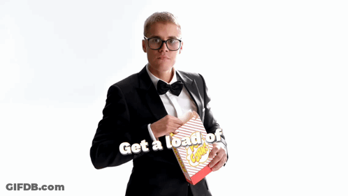 A Man In A Tuxedo Is Holding A Box Of Popcorn With The Words Get A Load Of This Guy Below Him GIF