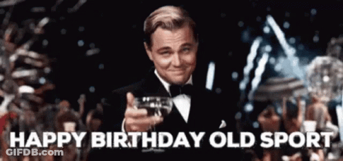 A Man In A Tuxedo Is Holding A Glass Of Wine In His Hand And Says Happy Birthday Old Sport . GIF