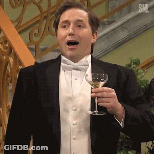 A Man In A Tuxedo Is Holding A Glass Of Wine In His Hand . GIF