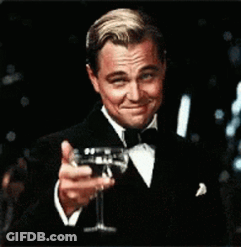 A Man In A Tuxedo Is Holding A Glass Of Wine In His Hand GIF
